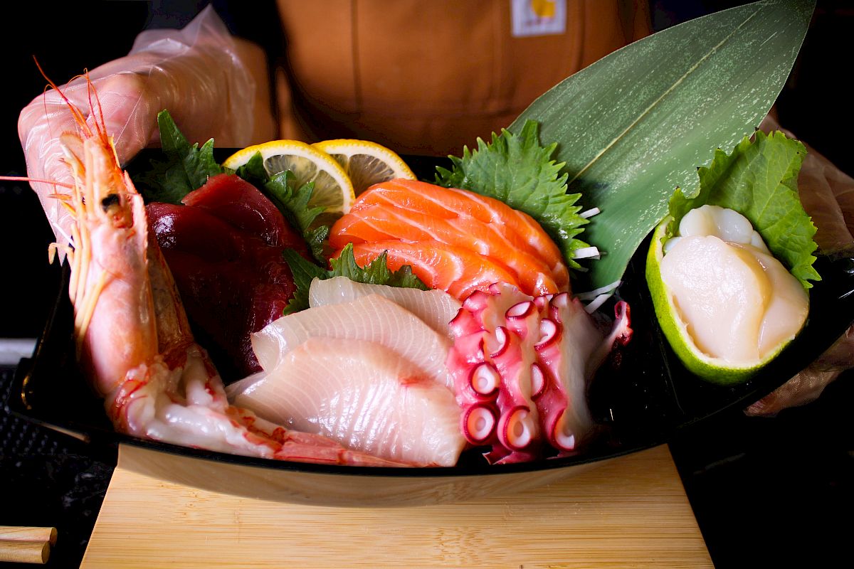 A vibrant sashimi platter featuring shrimp, salmon, octopus, and other seafood garnished with greens and lemon slices.