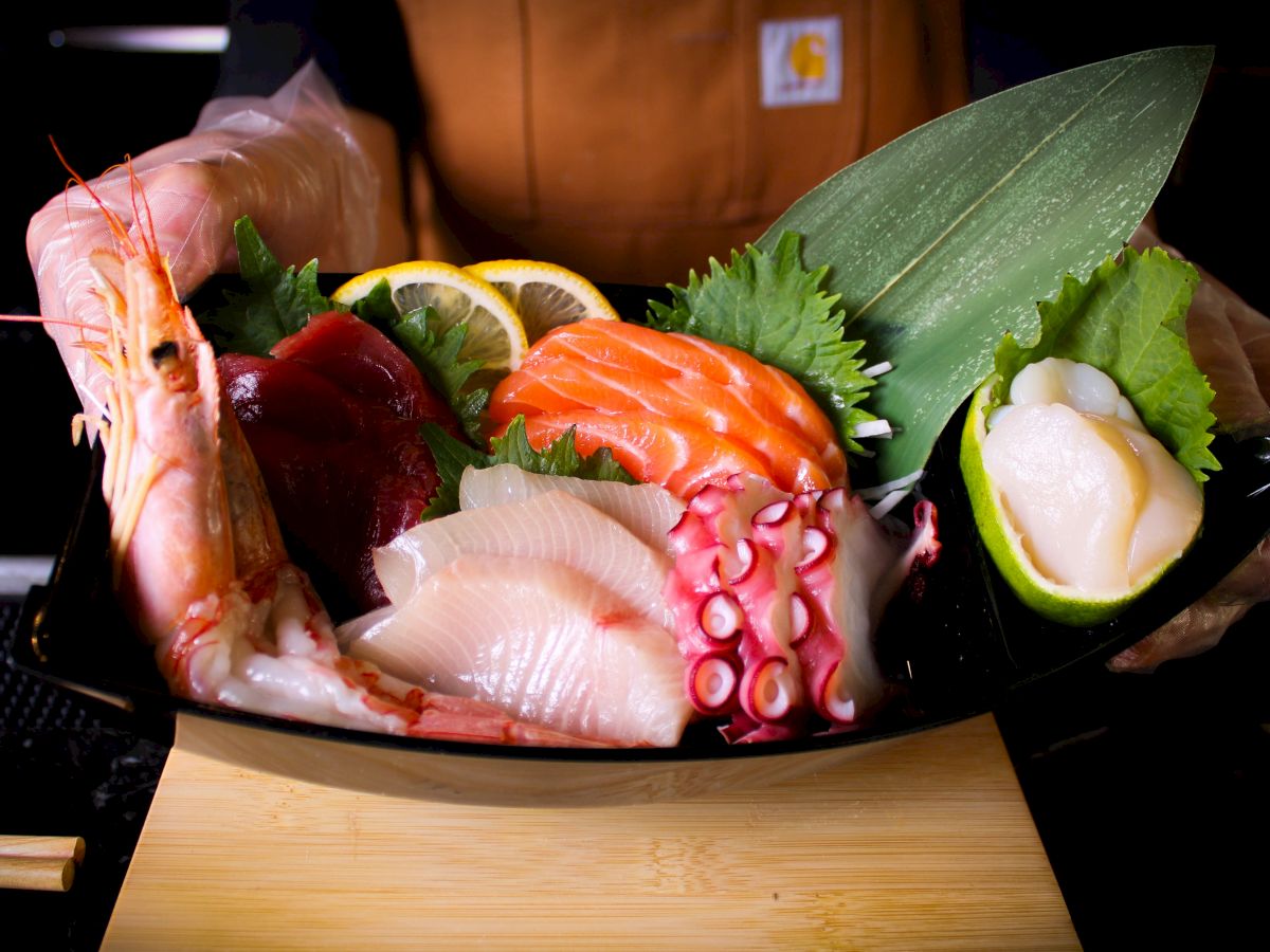 A vibrant sashimi platter featuring shrimp, salmon, octopus, and other seafood garnished with greens and lemon slices.