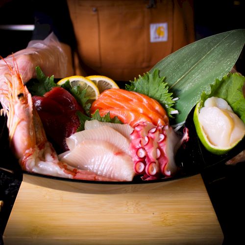 This image shows a platter of assorted sashimi, including shrimp, salmon, tuna, octopus, and garnishes like lemon slices and greens.