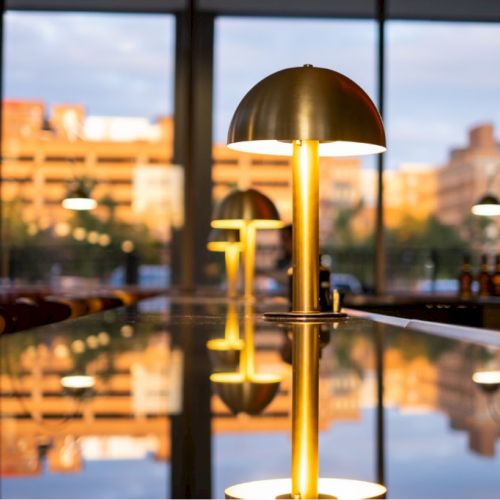 A modern indoor setting with stylish lamps and reflective surfaces, capturing a cityscape through large windows at sunset.